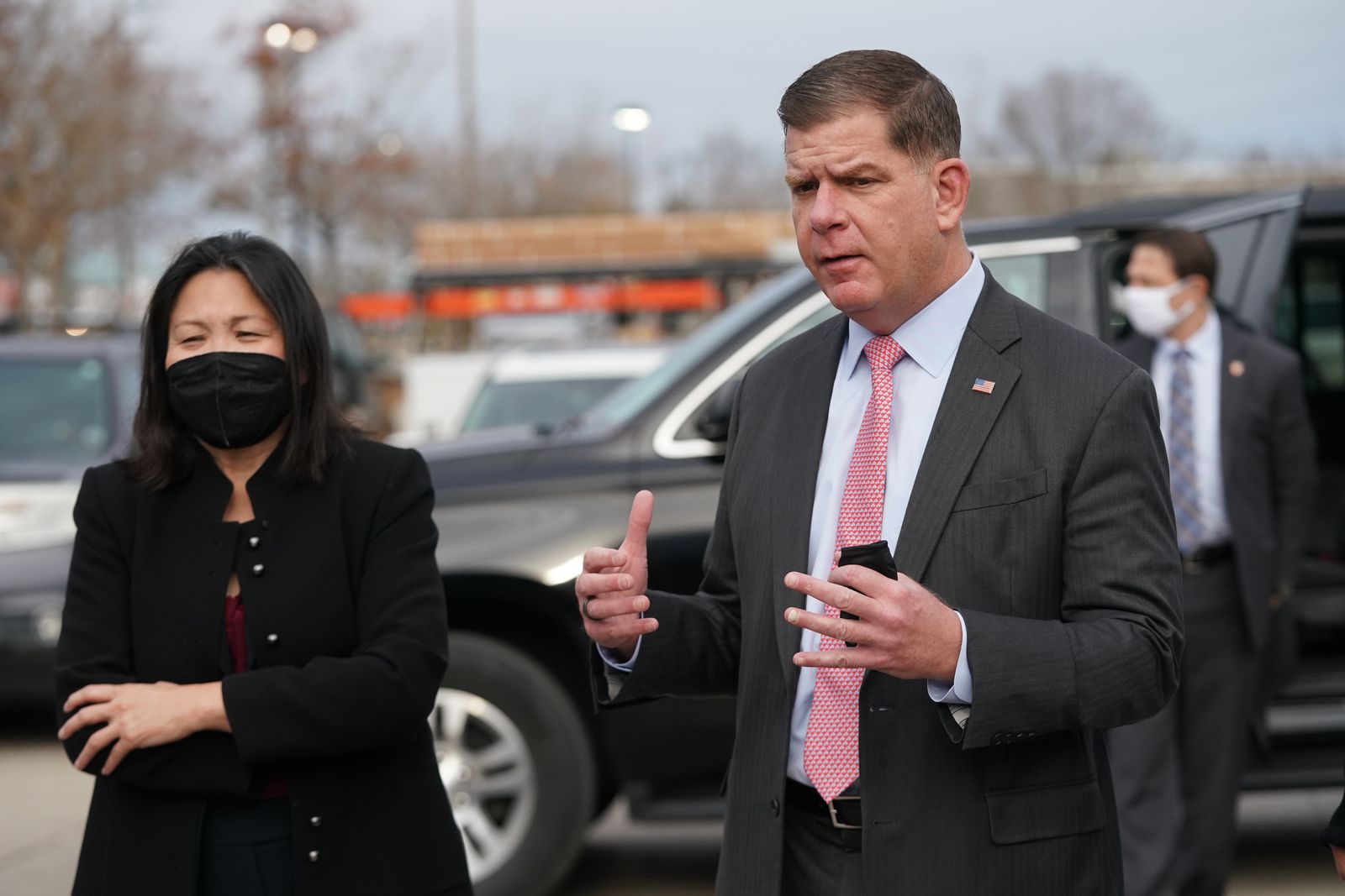 On the right, Marty Walsh stands in a black suit and red tie. To the left is Julie Su, who wears a black face mask and jacket.